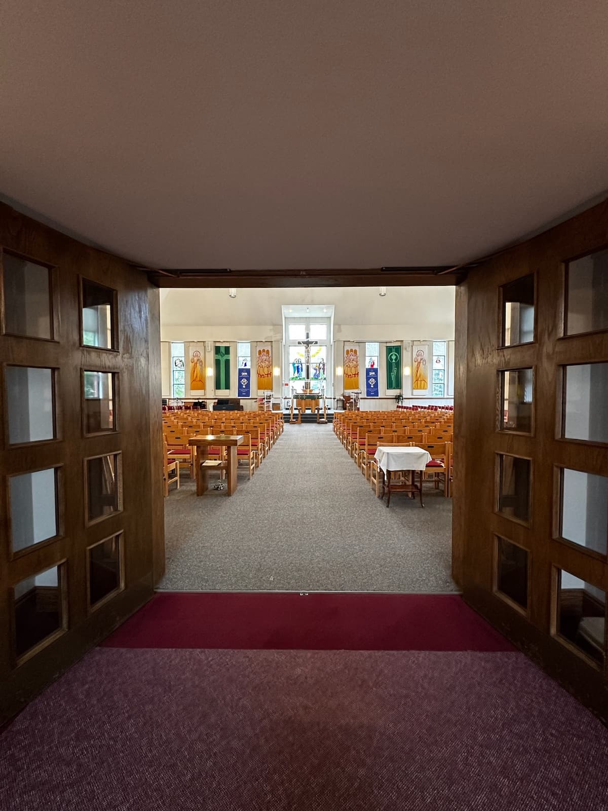 View down the central aisle toward the altar, with rows of seating on both sides and a crucifix window at the far end.
