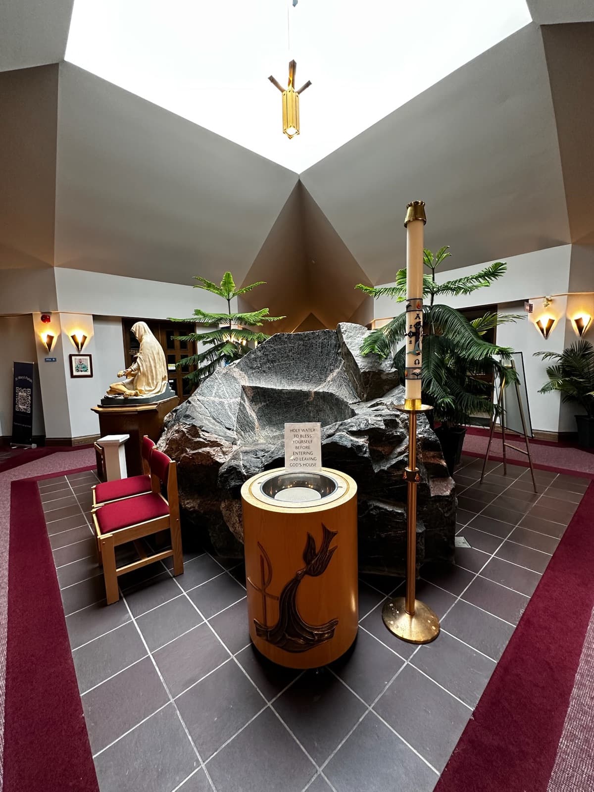 The carved wooden baptismal font, bearing a dove and Chi-Rho, beside the paschal candle and the parish's large natural rock.