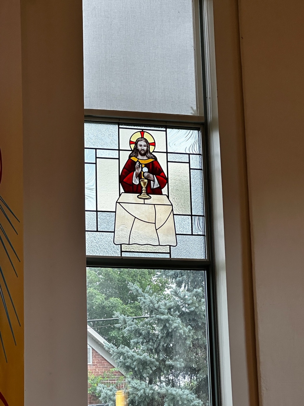 Stained-glass panel showing Christ in red vestments standing at a draped altar, raising the host above a golden chalice.